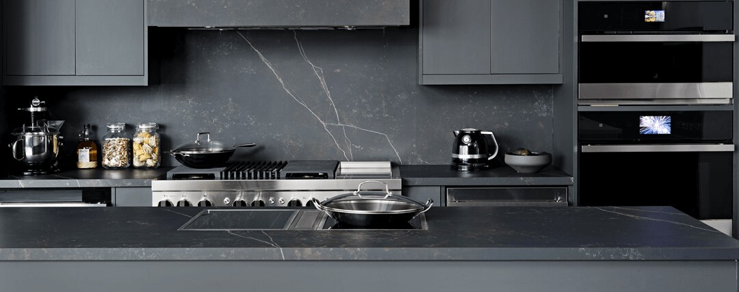 A JennAir Induction Cooktop installed in a dark, modern kitchen with other JennAir Brand appliances.  A JennAir Induction Cooktop installed in a dark, modern kitchen with other JennAir Brand appliances.